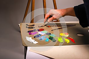 The hand of the artist works with paints. The artist stirs paints. The female hand of an elderly artist works with a palette knife