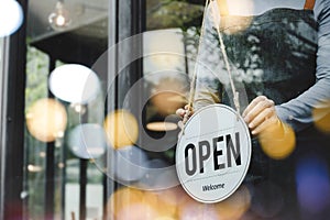 Hand of asain staff woman wearing apron turning open sign board on glass door in modern cafe coffee shop, hotel service, cafe rest