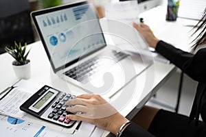 Hand of an Asian female employee is calculating numbers in the office. She was using a calculator on a white table