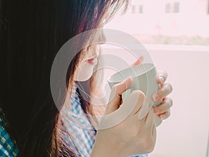 hand of asian girl in blue flannel shirt hold hot coffee for drink in morning time with soft focus foreground and background