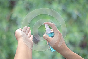 Hand of Asian woman applying the alcohol spray with greenery background. Closed up alcohol spray