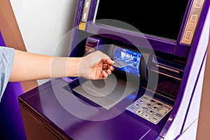 Hand of Asian woman inserting ATM card into ATM machine.