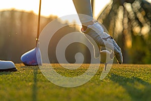 Hand asian woman putting golf ball on tee with club in golf course on evening and sunset time a for healthy sport.