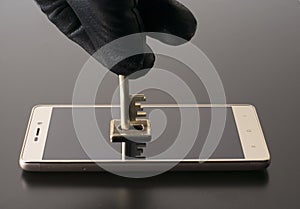 The hand of an attacker in a black glove opens the lock on a smartphone with a key. The concept of protecting personal information