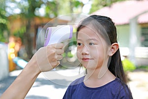 Hand of authorities with electronic infrared thermometer measuring asian little kid girl head before entering the playground