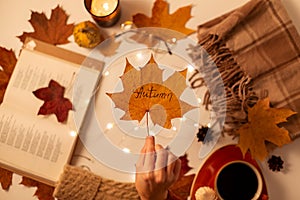 hand with autumn leaf, book, coffee and blanket