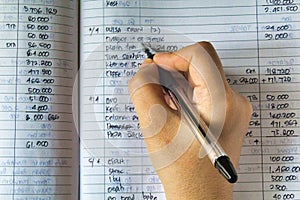Hand and ballpoint pen on a ledger book, writing down expenses and calculating the taxes