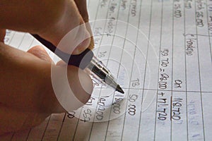 Hand and ballpoint pen on a ledger book, writing down expenses and calculating the taxes