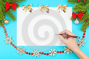 Hand with ballpoint pen over a white blank paper with Christmas border consisting of branches of spruce, christmas toys