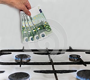 Hand with banknotes of 100 euros on the background of blue flame of a gas stove.