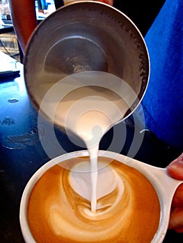Pouring latte art in white mug cream coffee espresso