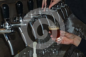 The hand of a bartender girl at a beer tap pours draft beer into a glass served in a restaurant or pub