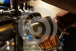 Hand of bartender pouring a large lager beer in tap. Rest in a bar with friends