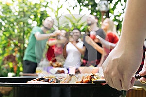 Hand of bbq grilling and friends having barbecue party, outdoors.