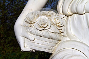 Hand of beautiful female marble statue with basker of rose flowers in hand close up on black background