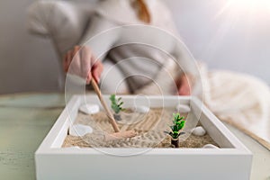 Hand of beautiful young woman using her Zen garden at home. Lovely young smiling woman relaxing with her Zen garden and enjoying