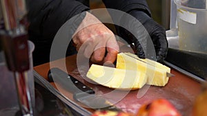 hand in black gloves cutting pineapple on a chopping board at street