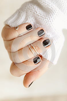hand with black manicure and rings on the phalanges on short nails in a white sweater on a light background. The concept of a