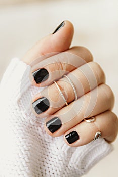 hand with black manicure and rings on the phalanges on short nails in a white sweater on a light background. The concept of a