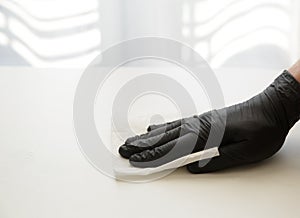 Hand in a black nitrile glove wipes the table with disinfectant solution