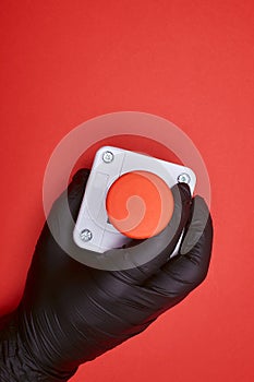 The hand in black resin glove, which constrict the emergency button at the red background photo