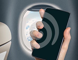 Hand with blank mobile phone in airplane or jet interior