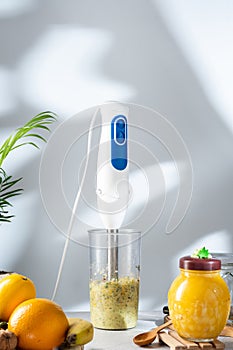 Hand blender on the table with food. Grinding fruit with a blender. Vertical frame.