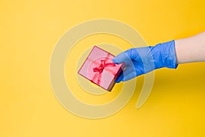 a hand in a blue disposable glove holds a red gift box with a bow from a red ribbon