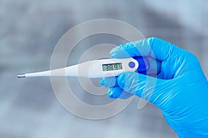 Hand in blue glove holding a digital thermometer on white background. Medical worker wearing protective gloves checking medical