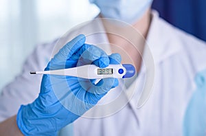 Hand in blue glove holding a digital thermometer on white background. Medical worker wearing protective gloves checking medical