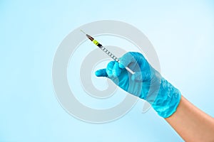 Hand in blue glove holding a plastic syringe with liquid for injection on light blue background. Health care, treatment