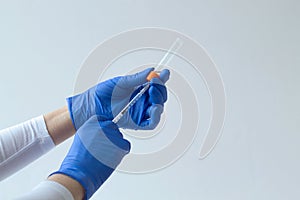 Hand in blue glove holding a syringe on grey background.