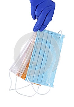 Hand in blue glove holds a colored medical face masks against viruses and bacteria on a white background.