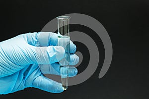 A hand in a blue glove holds a homeopathic remedy in a glass tube on a black background, close-up