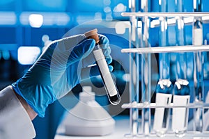 Hand in blue glove holds test tube in laboratory, symbolizing scientific analysis/experimentation