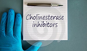 Hand in blue glove, pen, white note with words `cholinesterase inhibitors`. Beautiful blue background photo