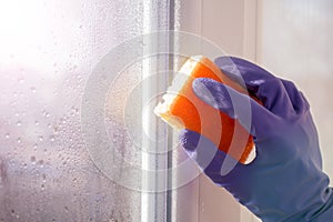 Hand blue glove washes window with yellow sponge