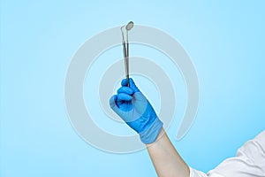 A hand in a blue medical glove holds dental instruments on a light blue background. Dentistry concept.