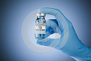 Hand in blue medical gloves holding a vaccine vial with Covid 19 Vaccine Booster text, for Coronavirus booster shot