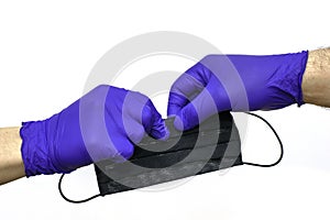 Hand in a blue medical protective glove transfers a black medical mask to another gloved hand on the white background