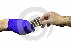 The hand in a blue medical surgical glove transfers a blister with pills to an unprotected hand