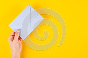 Hand with blue paper envelope composition on yellow background