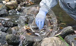 Hand in blue in a protective glove, pours liquid from a test tube into a riverbed