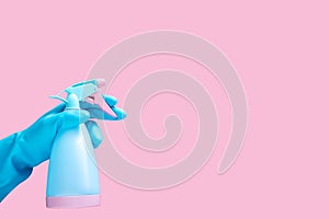 Hand in blue rubber glove holding cleaning spray bottle detergent isolated on pink background with copy space for text or logo