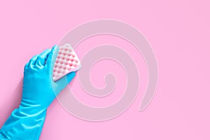 Hand in blue rubber glove holding pink cleaning sponge isolated on pink background with copy space for text or logo.