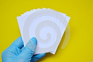 A hand in a blue rubber glove holds a white blank paper on a yellow background
