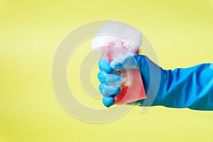 Hand in blue rubber glove squeezing red sponge with foam.