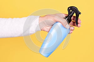 Hand with blue sun protection spray bottle. Isolated on yellow background