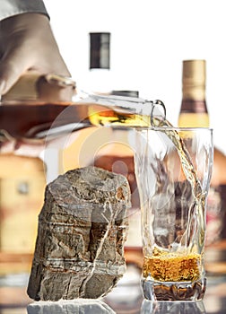 Hand with a bottle filling a transparent glass with alcohol