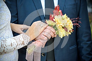 Hand of bride and groom. Bride and groom hold hands. Focus on the rings. Bouquet in hand